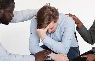 Distressed man being comforted by colleagues at work